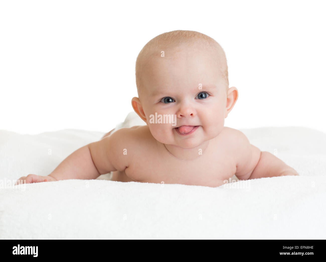 Cute smiling baby showing tongue lying on white towel Stock Photo