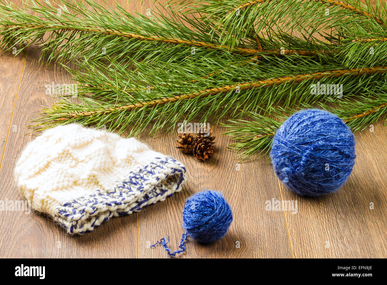 ball of threads, knitting cap, pine-cones and branch of pine on wooden ...
