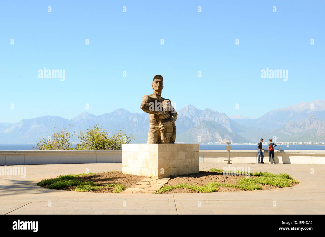 Statue of man protecting child, in public square with view of sea and mountains, Antalya, Turkey Stock Photo