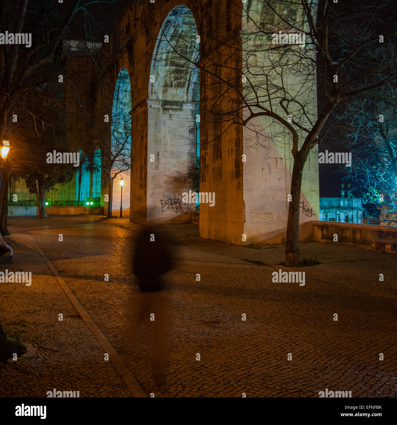 Night photography of a street with big stone arches in one side and a ghosted person. Stock Photo
