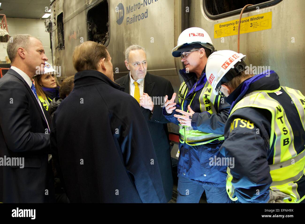 US Senator Chuck Schumer (center) is briefed by NTSB accident investigators as he visits the charred wreckage of a Metro North train car that collided with an SUV killing six people and injuring 12 others injured February 6, 2015 in New York's Westchester county. Stock Photo