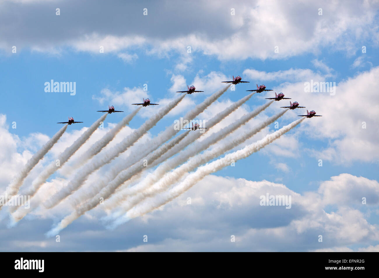 The Red Arrows world famous flying acrobatic team in classic arrowhead formation flypast trailing traditional coloured smoke Stock Photo