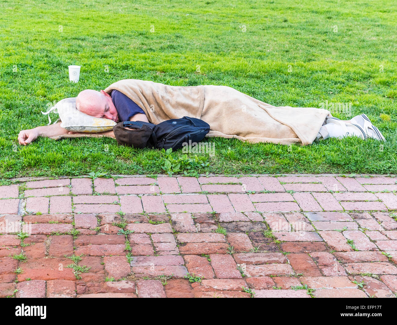 A homeless man sleeps lying down outside on the grass in front of the
