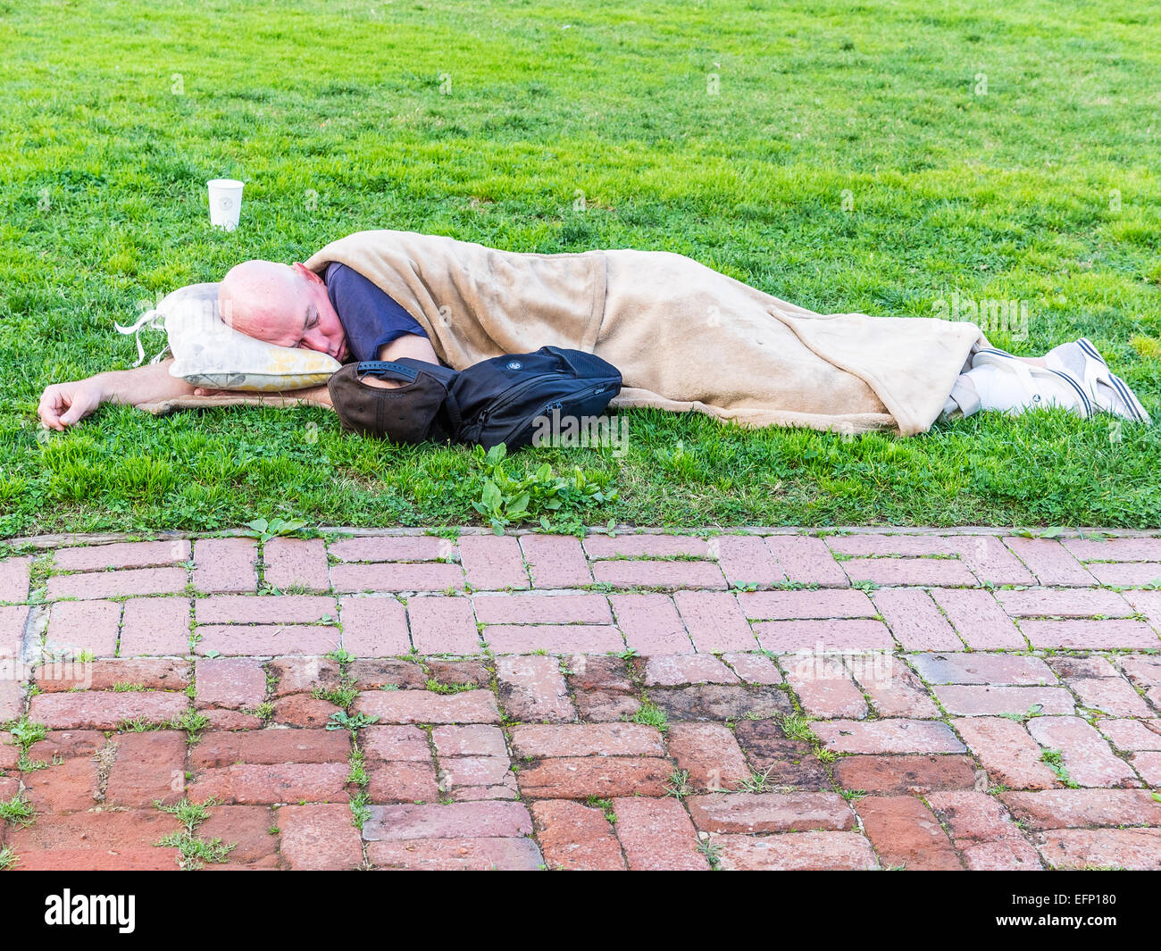 A homeless man sleeps lying down outside on the grass in front of the city hall in Santa Barbara, California. Stock Photo
