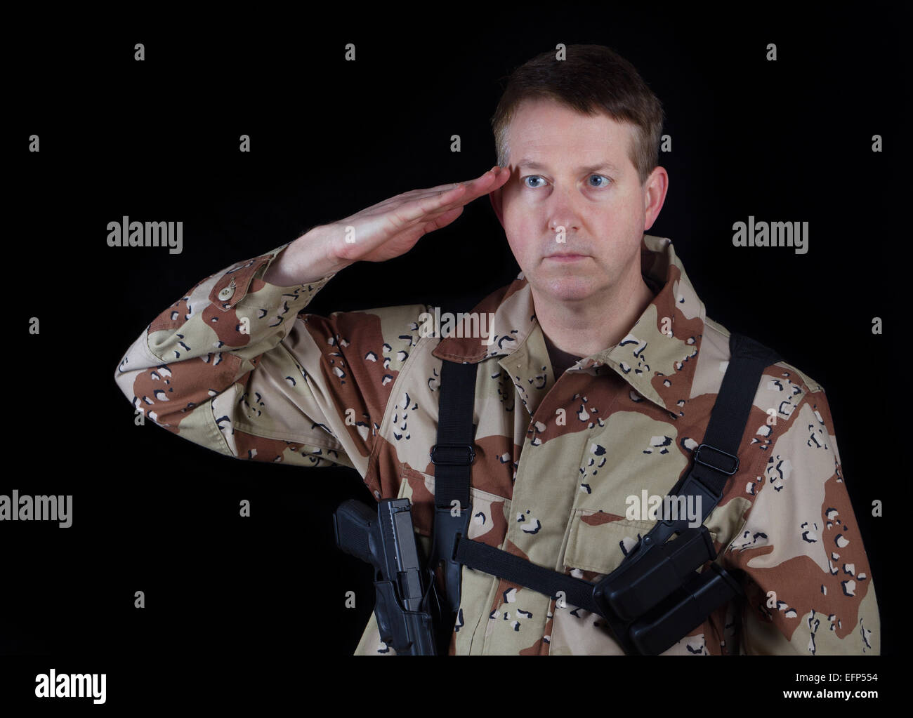 Horizontal image of military male soldier, head gear removed, saluting while armed with black background. Stock Photo