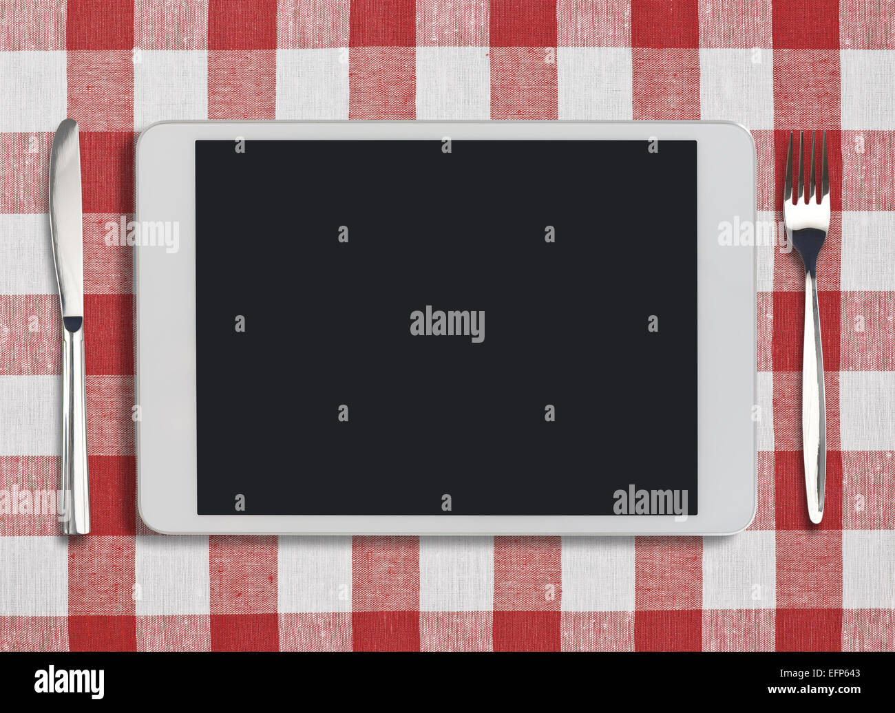 tablet pc, fork and knife on red checked tablecloth Stock Photo