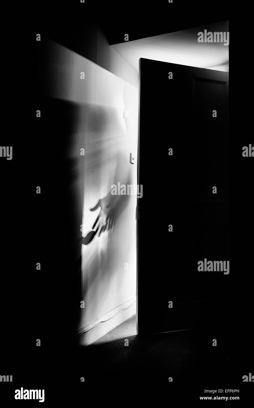 Shadow of a man opening a door into a dark room at night. Monochrome Stock Photo