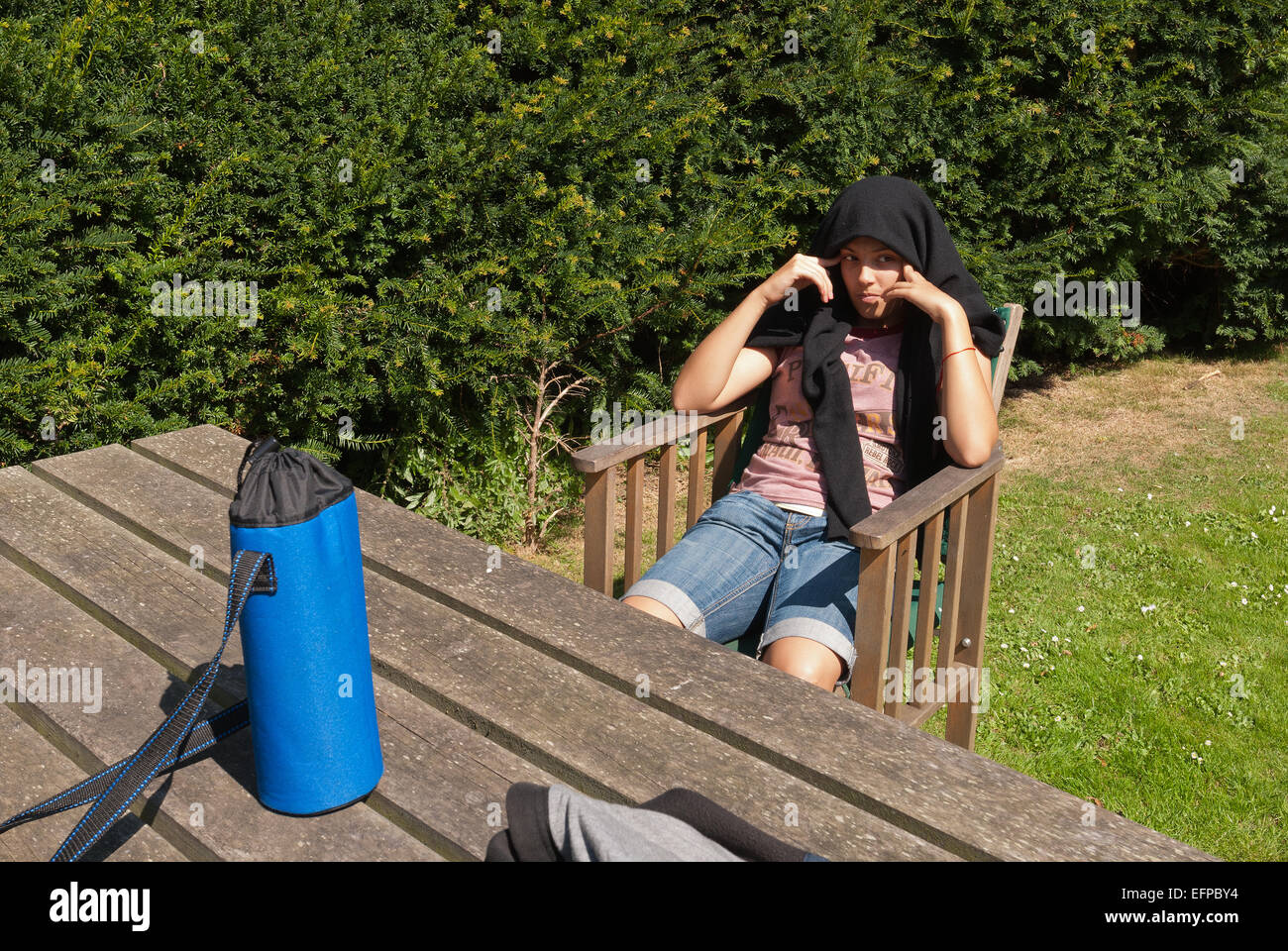 Head with jumper over head young teenager sitting at a wooden table in summer chair wants to be left alone Stock Photo