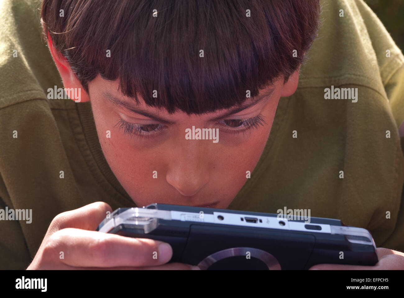 Intensive concentration and engagement with portable games console playing games outside looking at screen Stock Photo