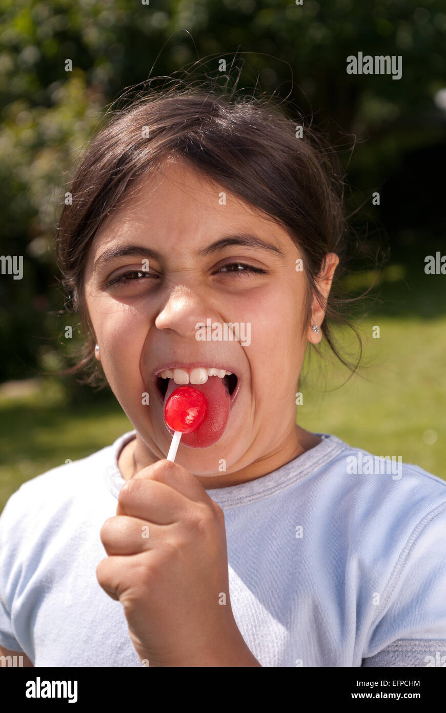 Happy child young girl outside sucking lollipop sweet on a paper handle need to look after teeth due sugar Stock Photo