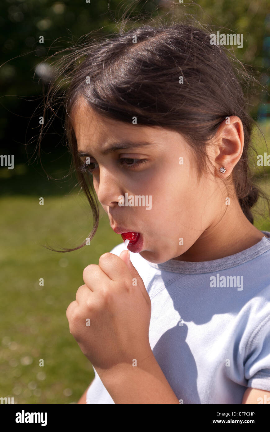 Happy child young girl outside sucking lollipop sweet on a paper handle need to look after teeth due sugar Stock Photo