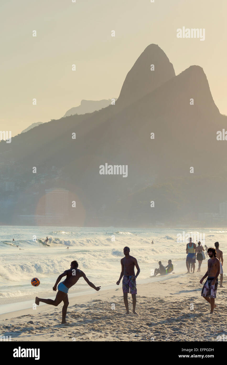 Locals playing football on Ipanema beach with the Morro dos Dois Irmaos (Two Brothers) mountains behind, Rio de Janeiro, Brazil Stock Photo