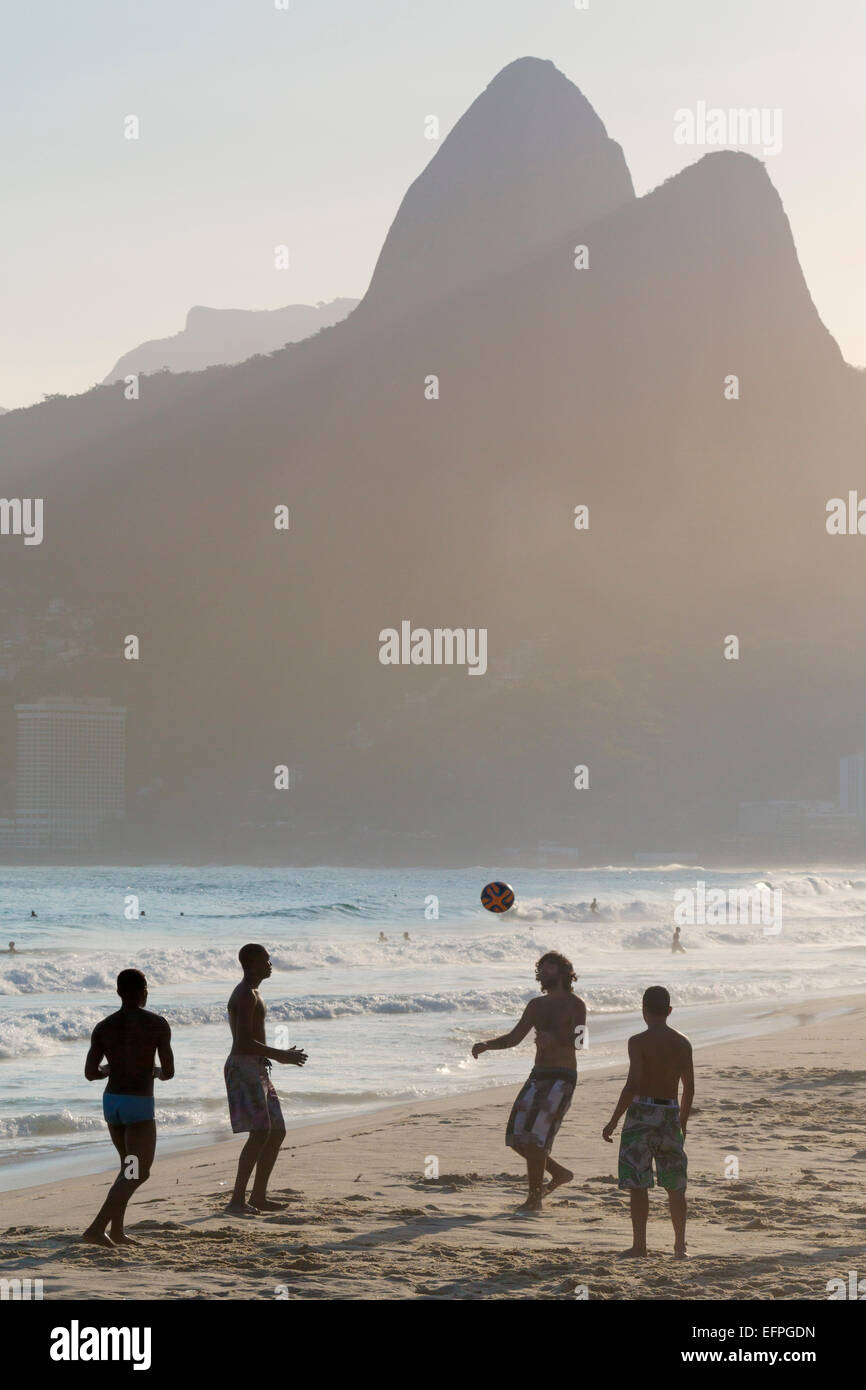 Locals playing football on Ipanema beach with the Morro dos Dois Irmaos (Two Brothers) mountains behind, Rio de Janeiro, Brazil Stock Photo