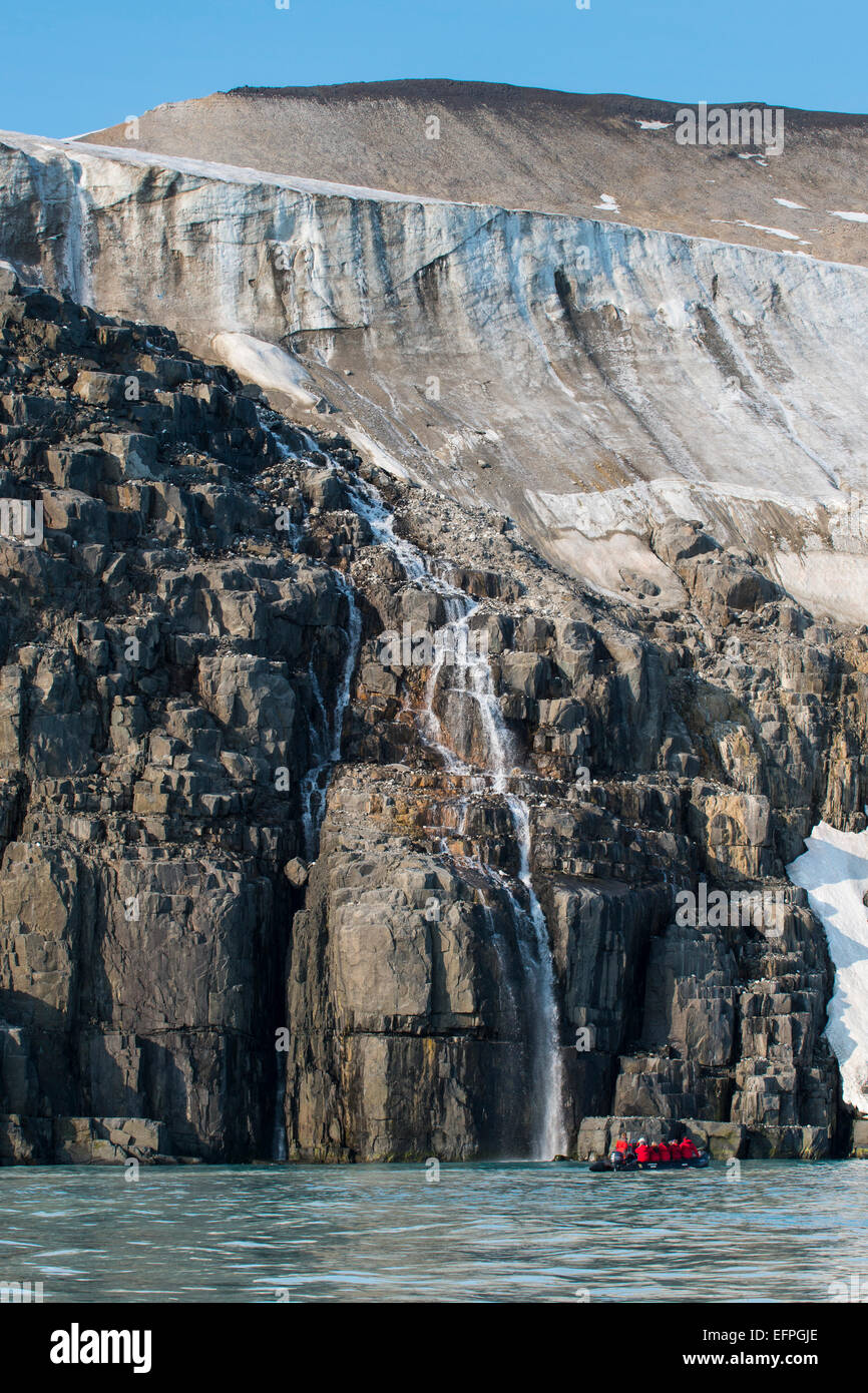 Tourist in a zodiac looking at Waterfall dropping in the ocean, Alkerfjellet, Svalbard, Arctic Stock Photo