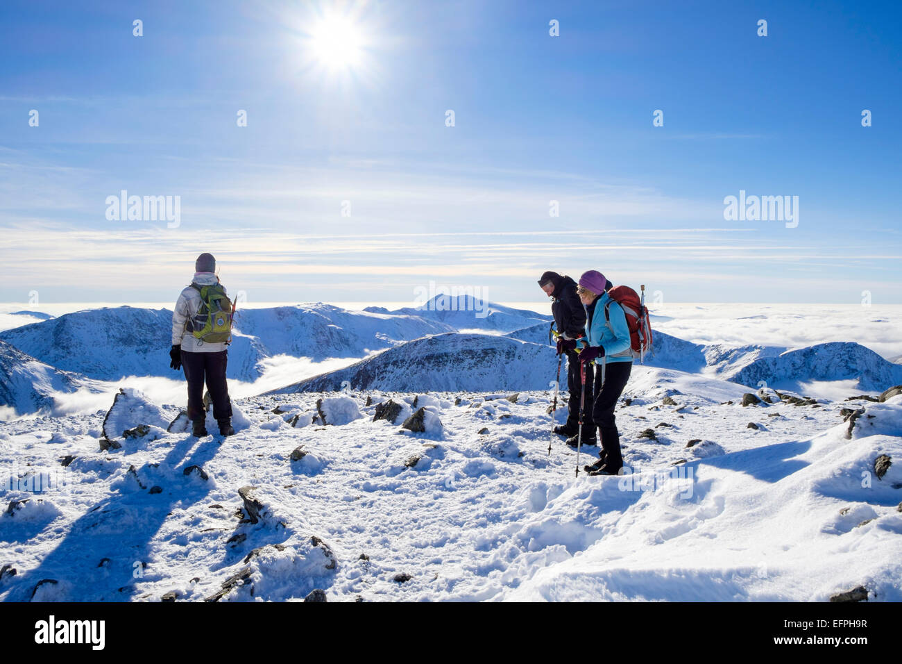 Hikers hiking on Carnedd Dafydd with view south to peaks above low cloud due to temperature inversion in winter sunshine. Snowdonia (Eryri) Wales UK Stock Photo