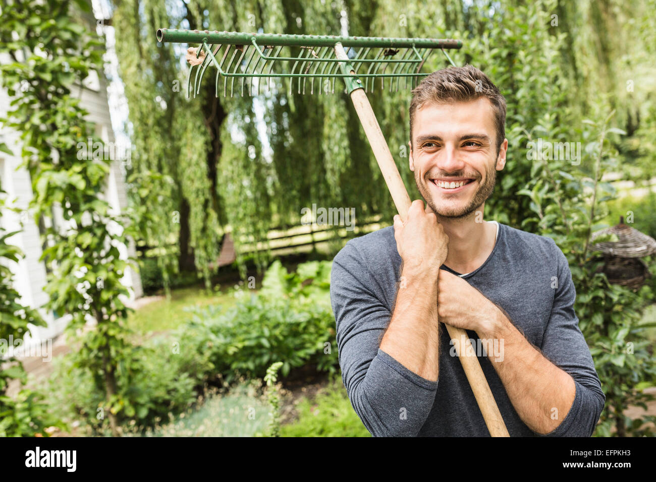 Young man holding rake Stock Photo Alamy