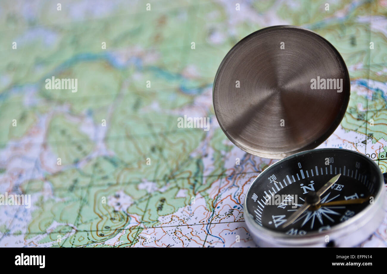The magnetic compass is located on a topographic map. Equipment for travel - map and compass. Stock Photo