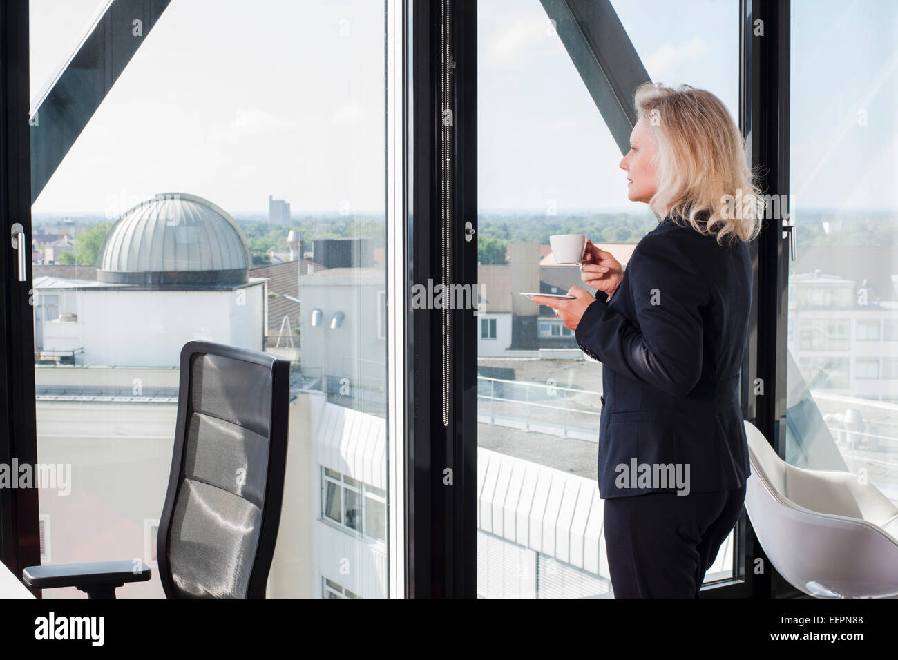 Businesswoman drinking coffee by window Stock Photo