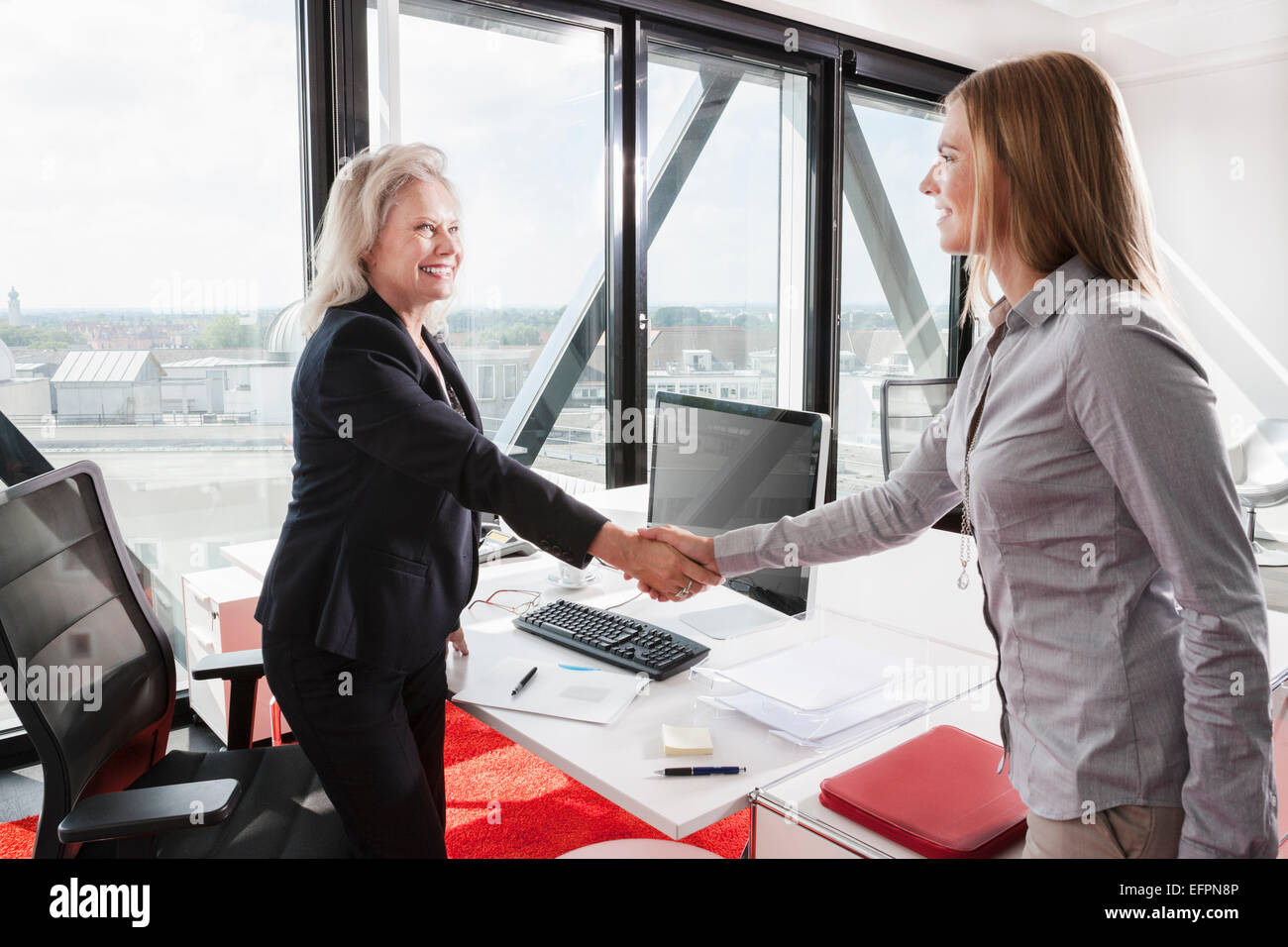 Two women shaking hands in office Stock Photo