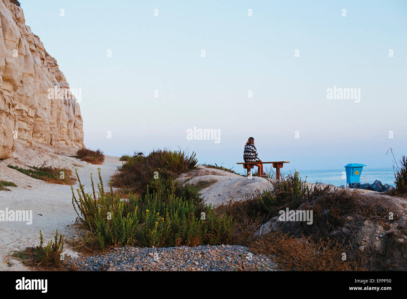 Young woman sitting on clifftop bench looking out to sea, San Clemente, California, USA Stock Photo