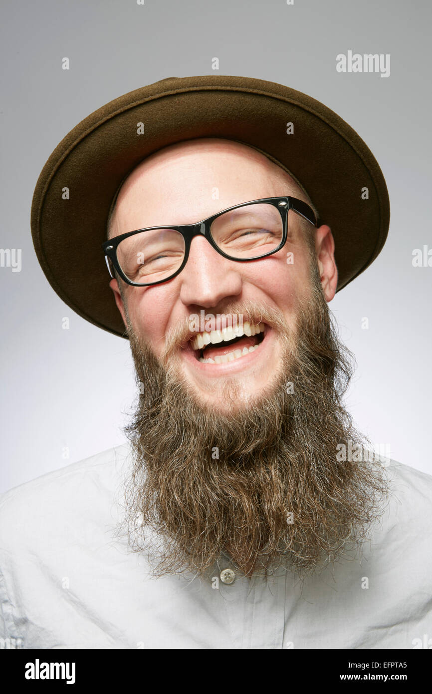 Studio portrait of laughing mid adult man in trilby with overgrown beard Stock Photo