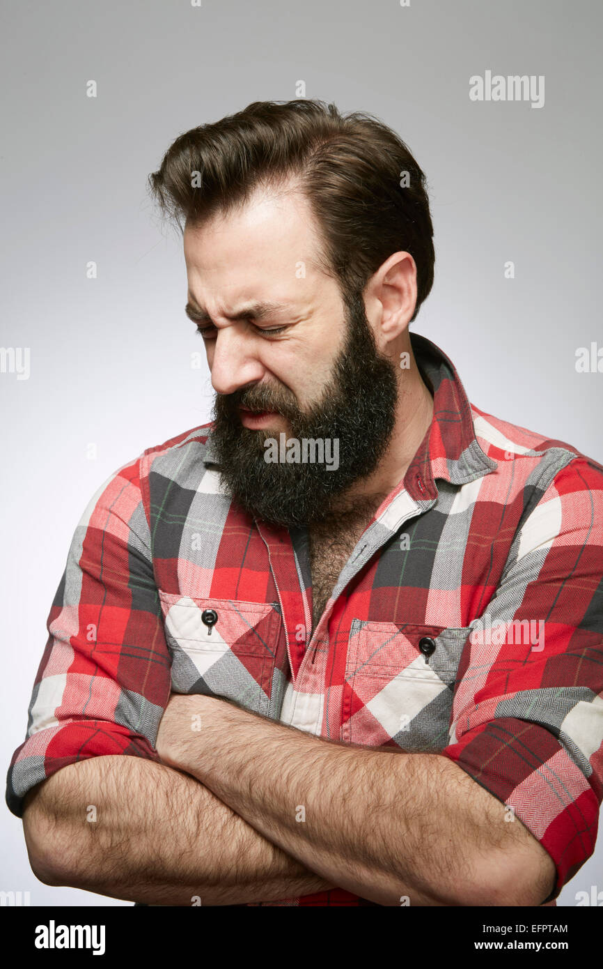 Studio portrait of anguished bearded young man with arms folded Stock Photo