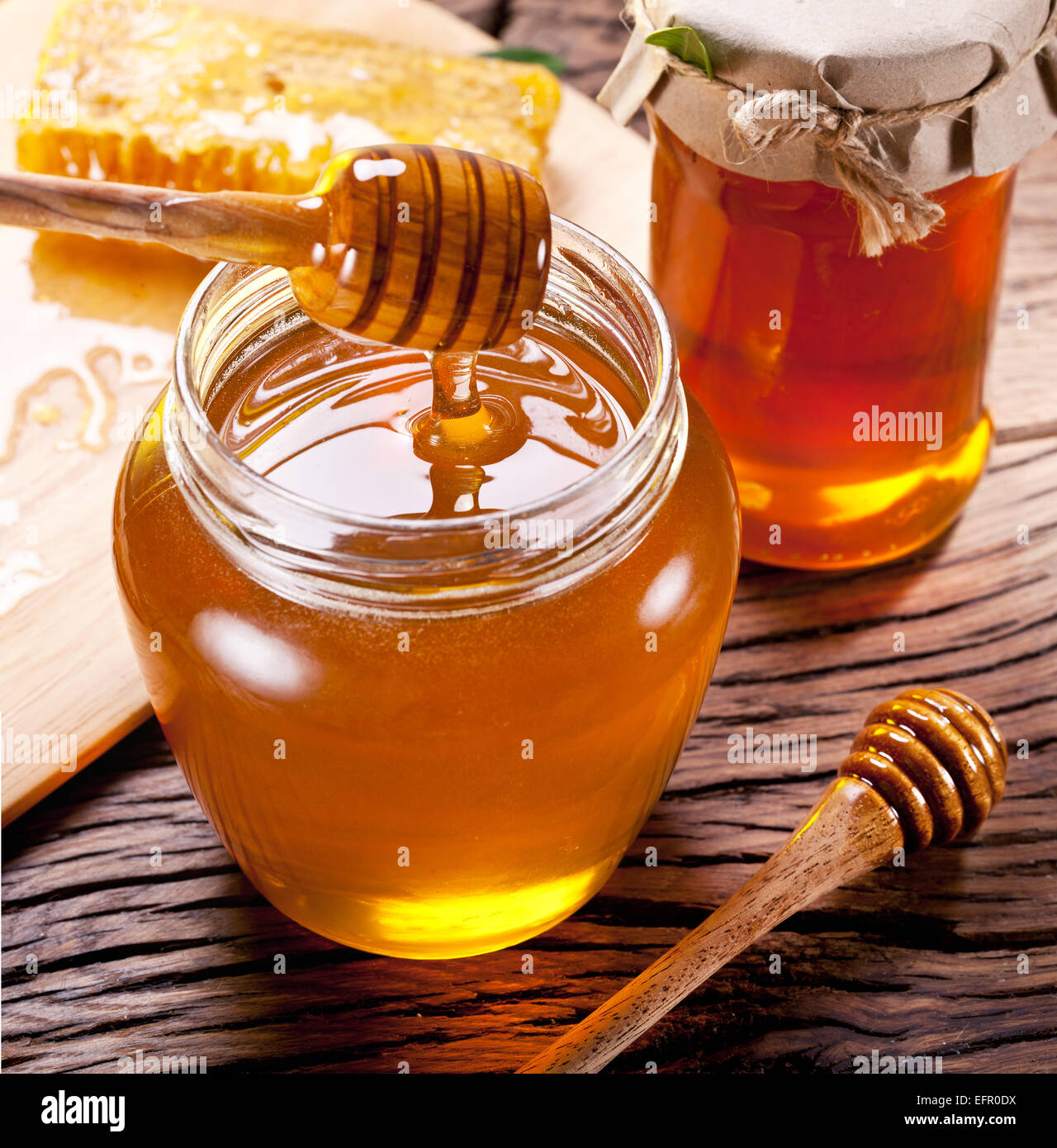 Honey dripping from wooden spoon into glass can. Stock Photo