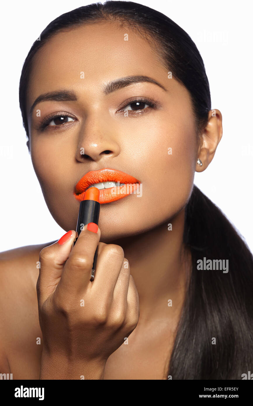 Female model applying orange lipstick Stock Photo