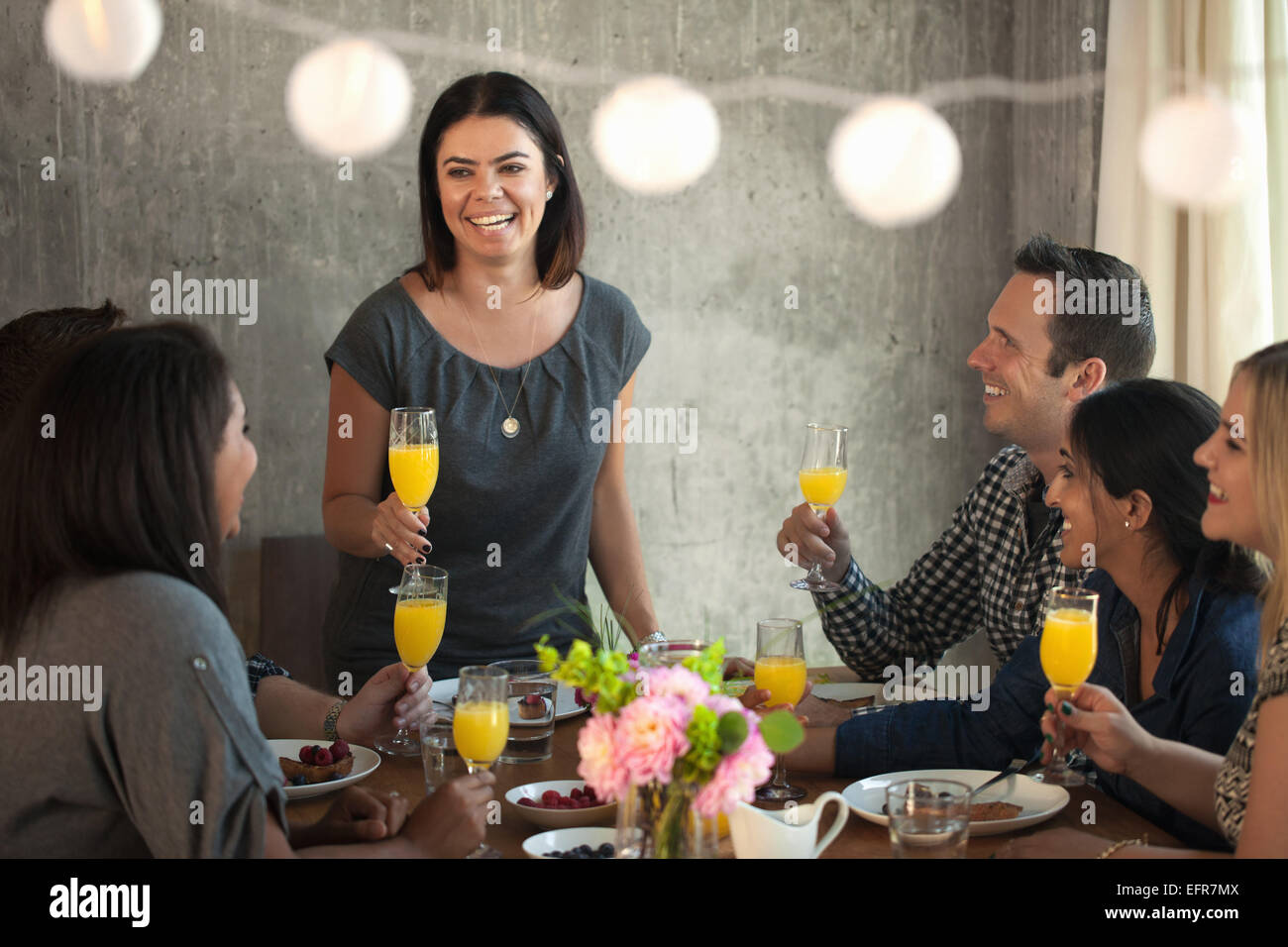 Group of friends at dinner table, young woman making toast Stock Photo