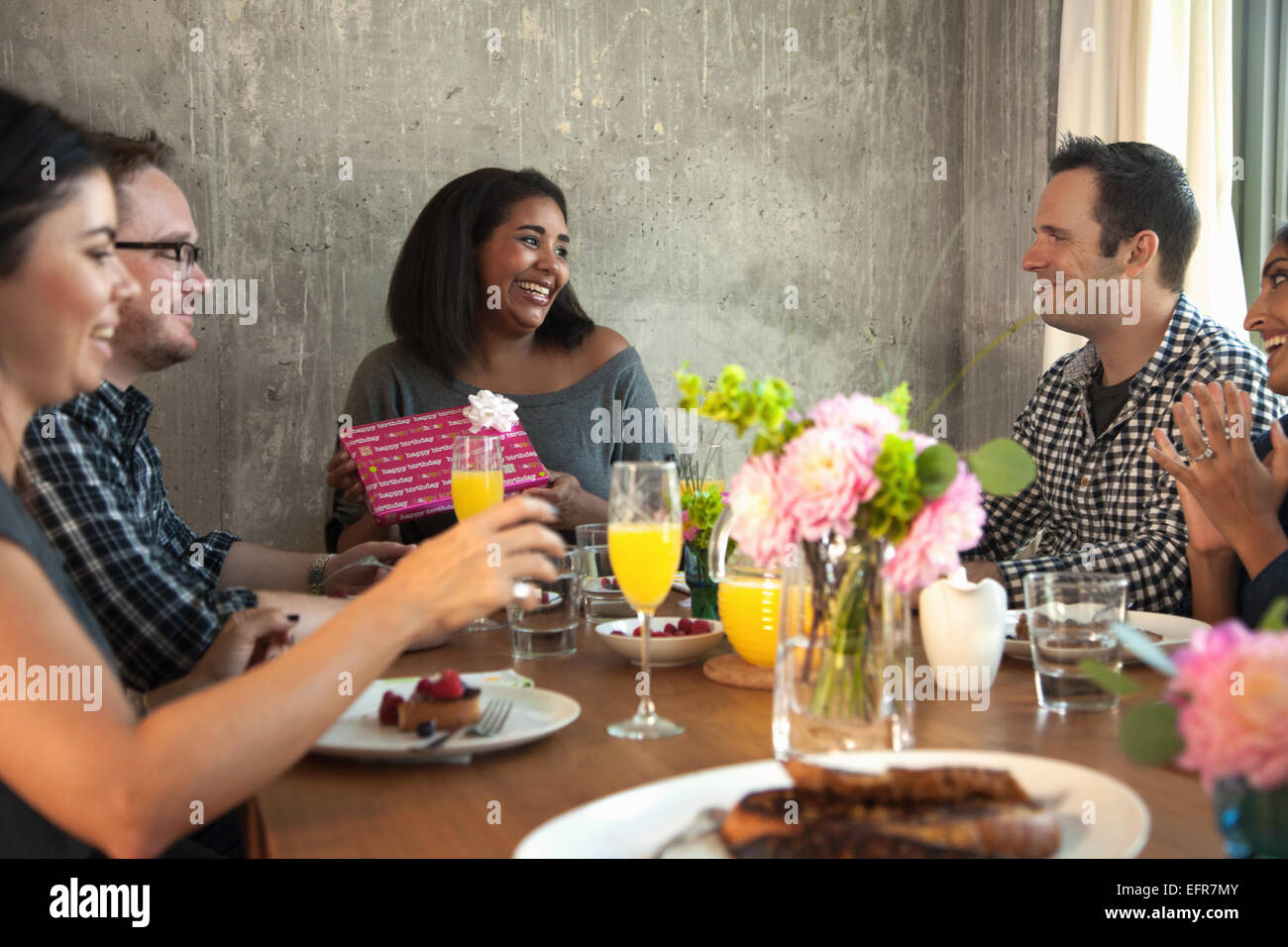 Group of friends at dinner table, Young woman holding wrapped gift Stock Photo