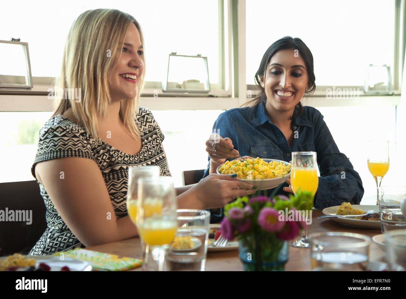 Group of friends having meal at table, young woman passing plate to friend Stock Photo