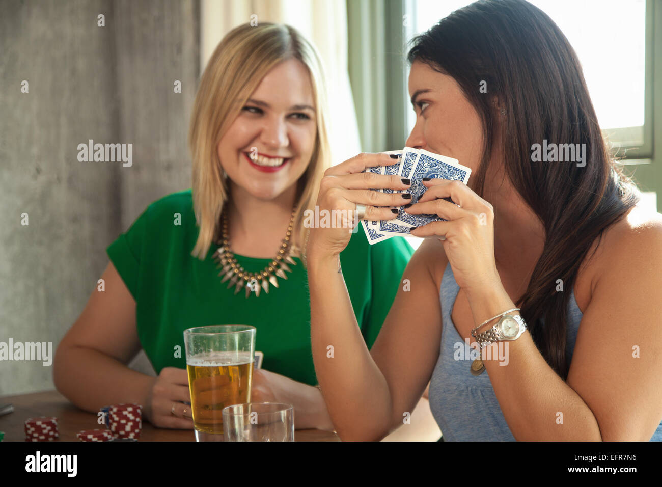 Two female friends playing cards, and laughing, at table Stock Photo