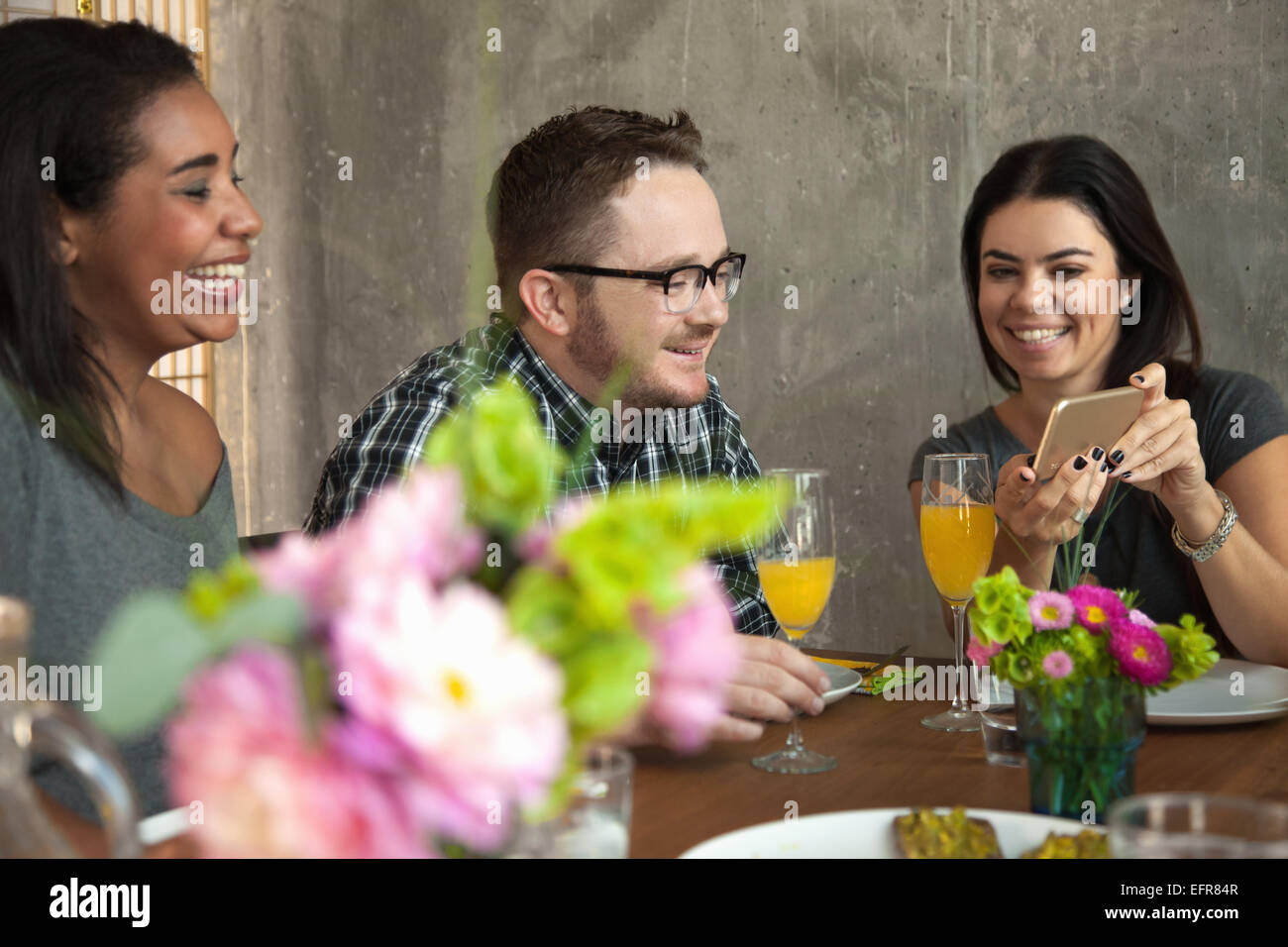 Friends at dinner table, young woman showing friend smartphone screen Stock Photo