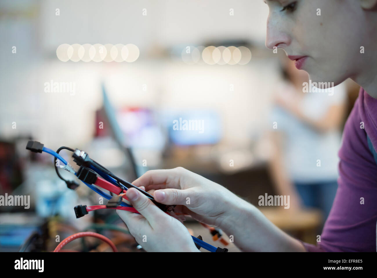 A young woman using connecting cables and usb leads in a computer repair shop. Stock Photo