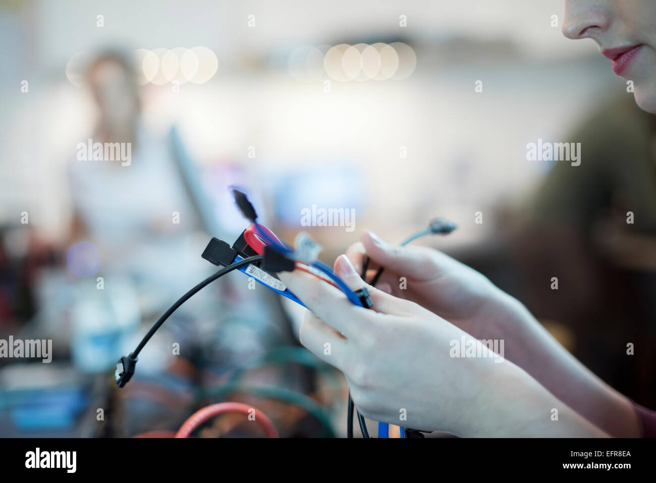 A young woman using connecting cables and usb leads in a computer repair shop. Stock Photo
