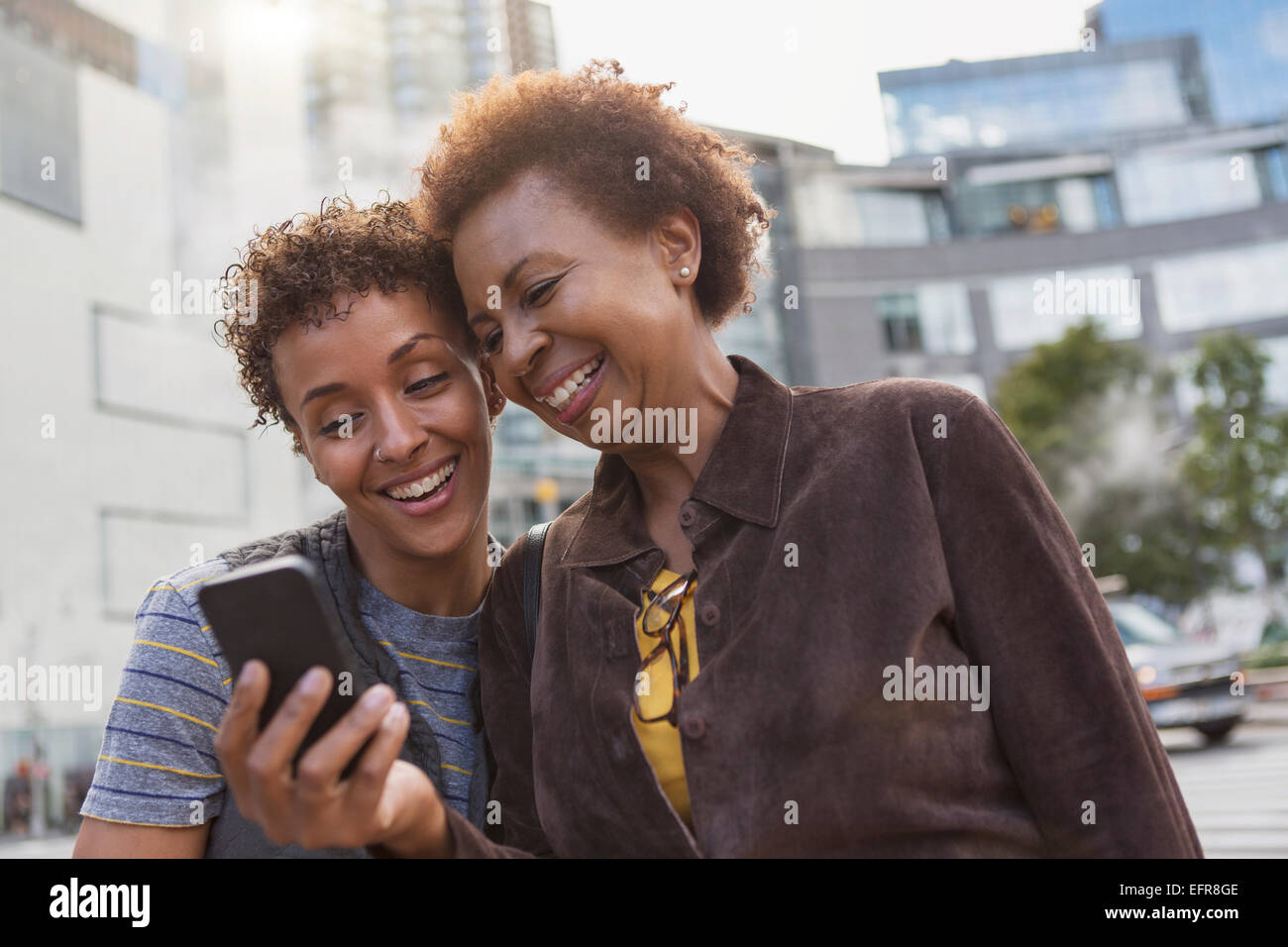 Two mature female friends laughing at smartphone texts on street Stock Photo
