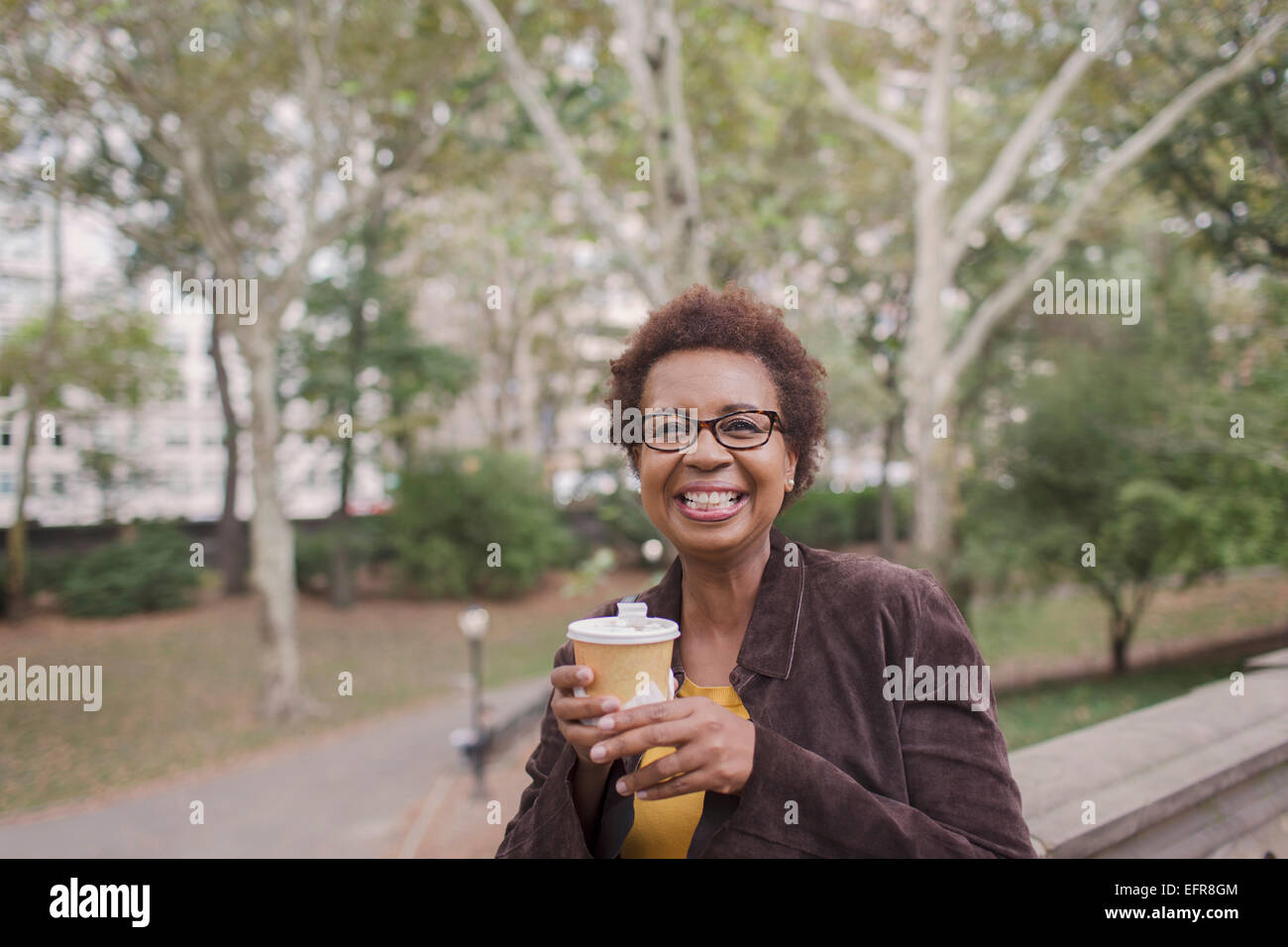 Portrait of smiling mature woman drinking takeaway coffee in park Stock Photo