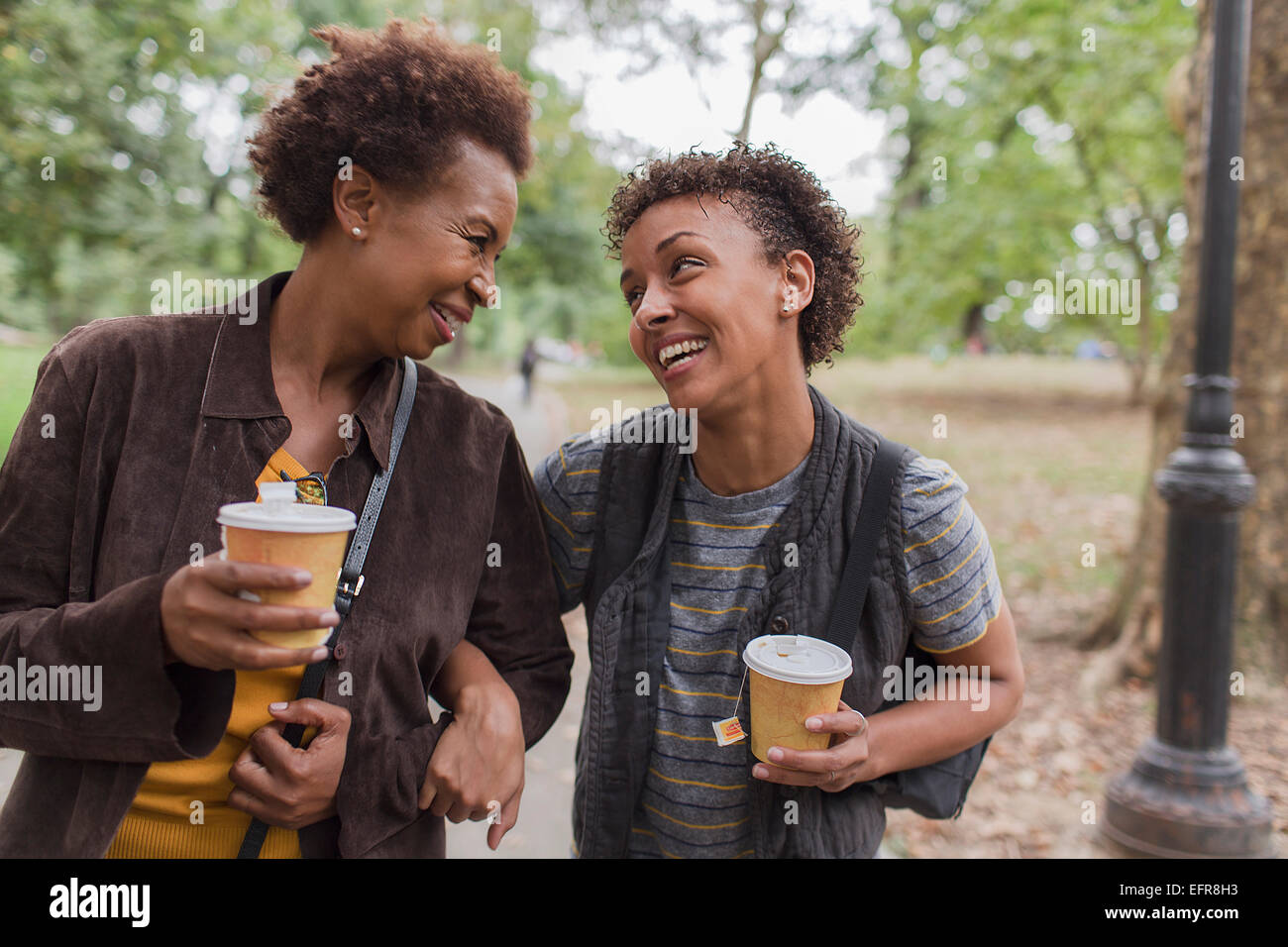 Two mature female friends drinking takeaway coffee whilst strolling  in park Stock Photo