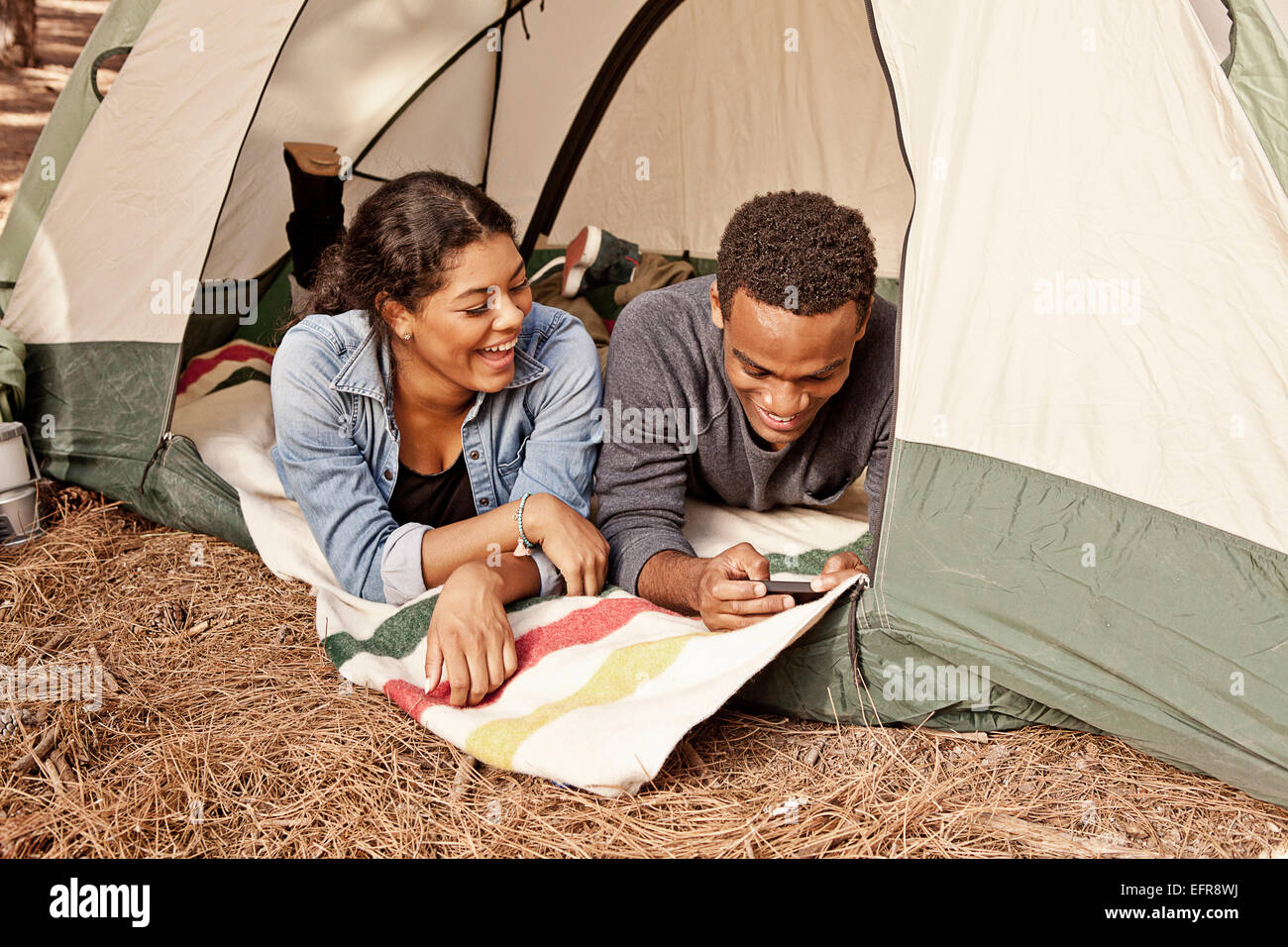 Young couple lying in tent entrance reading texts on smartphone Stock Photo
