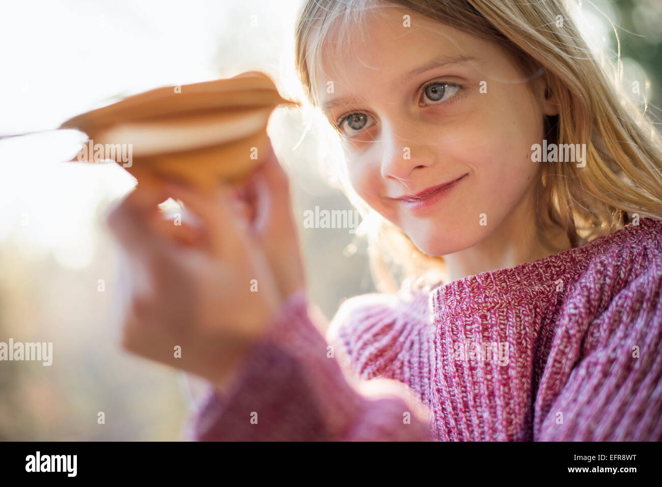 Blond girl standing in a forest in autumn, holding up and looking at a paper bird. Stock Photo