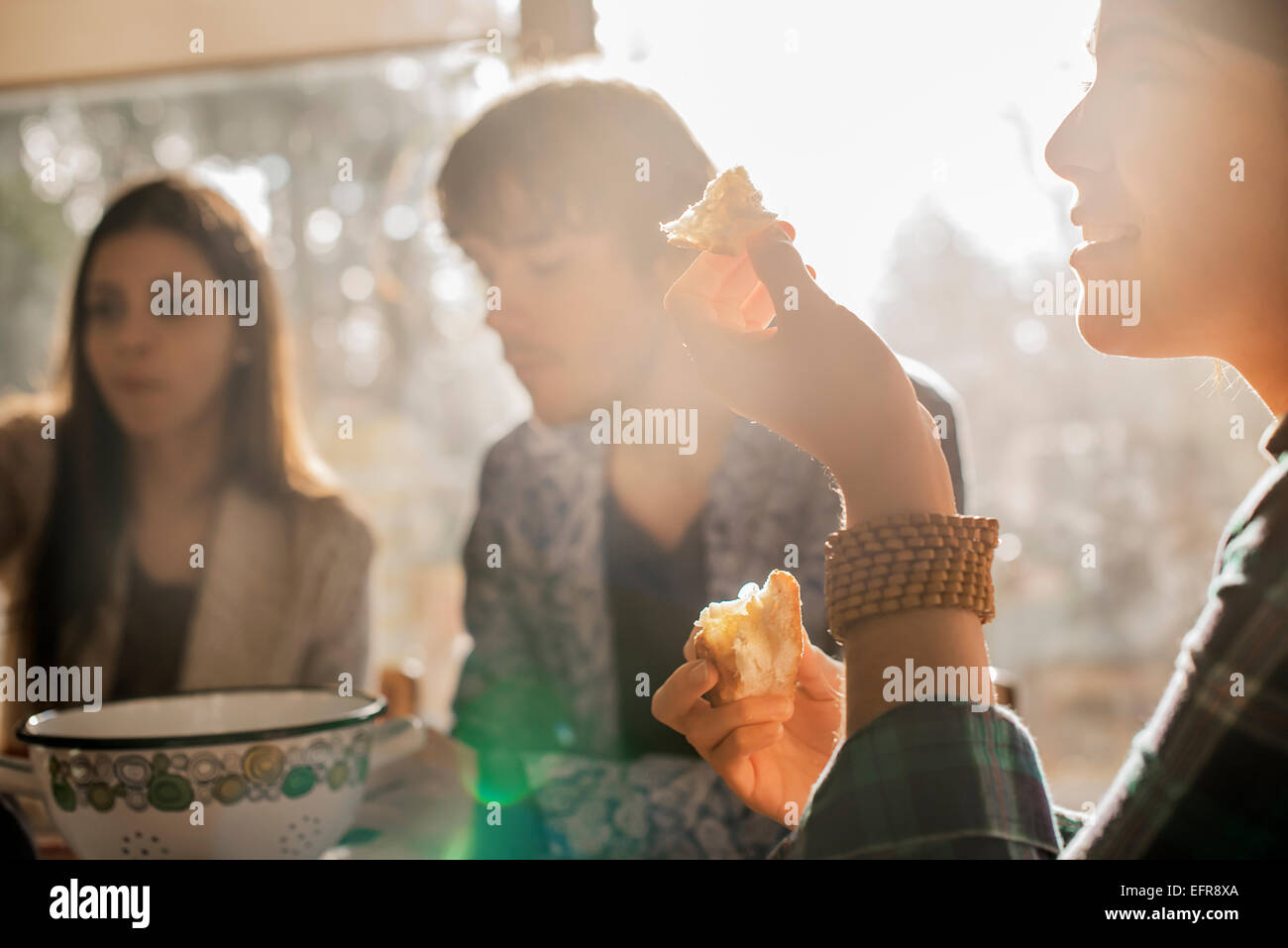 Three people sitting at a table, smiling, eating and chatting. Stock Photo