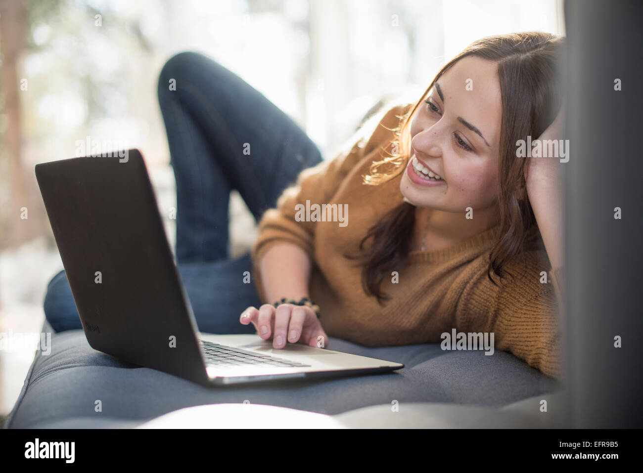 Woman lying on a sofa looking at her laptop, smiling. Stock Photo