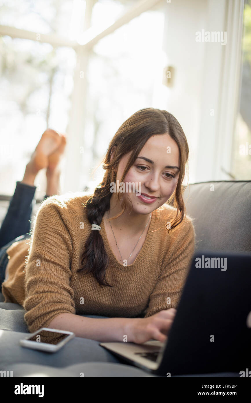 Woman lying on a sofa looking at her laptop, smiling Stock Photo - Alamy