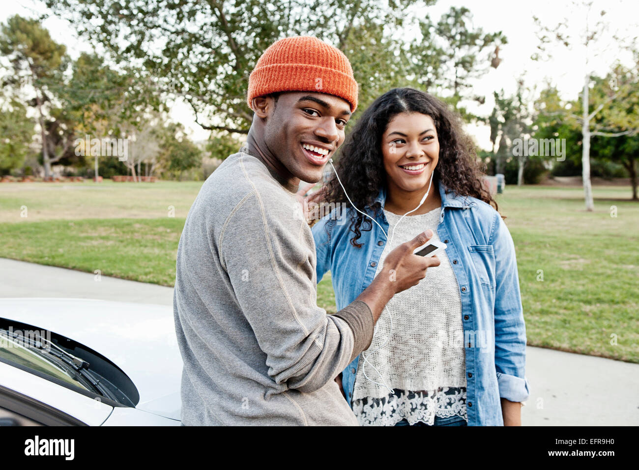 Portrait of young couple in car park sharing smartphone music Stock Photo