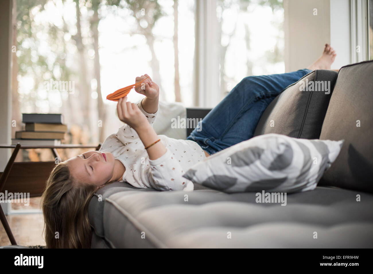 Girl lying on a sofa on her back, holding a paper bird. Stock Photo