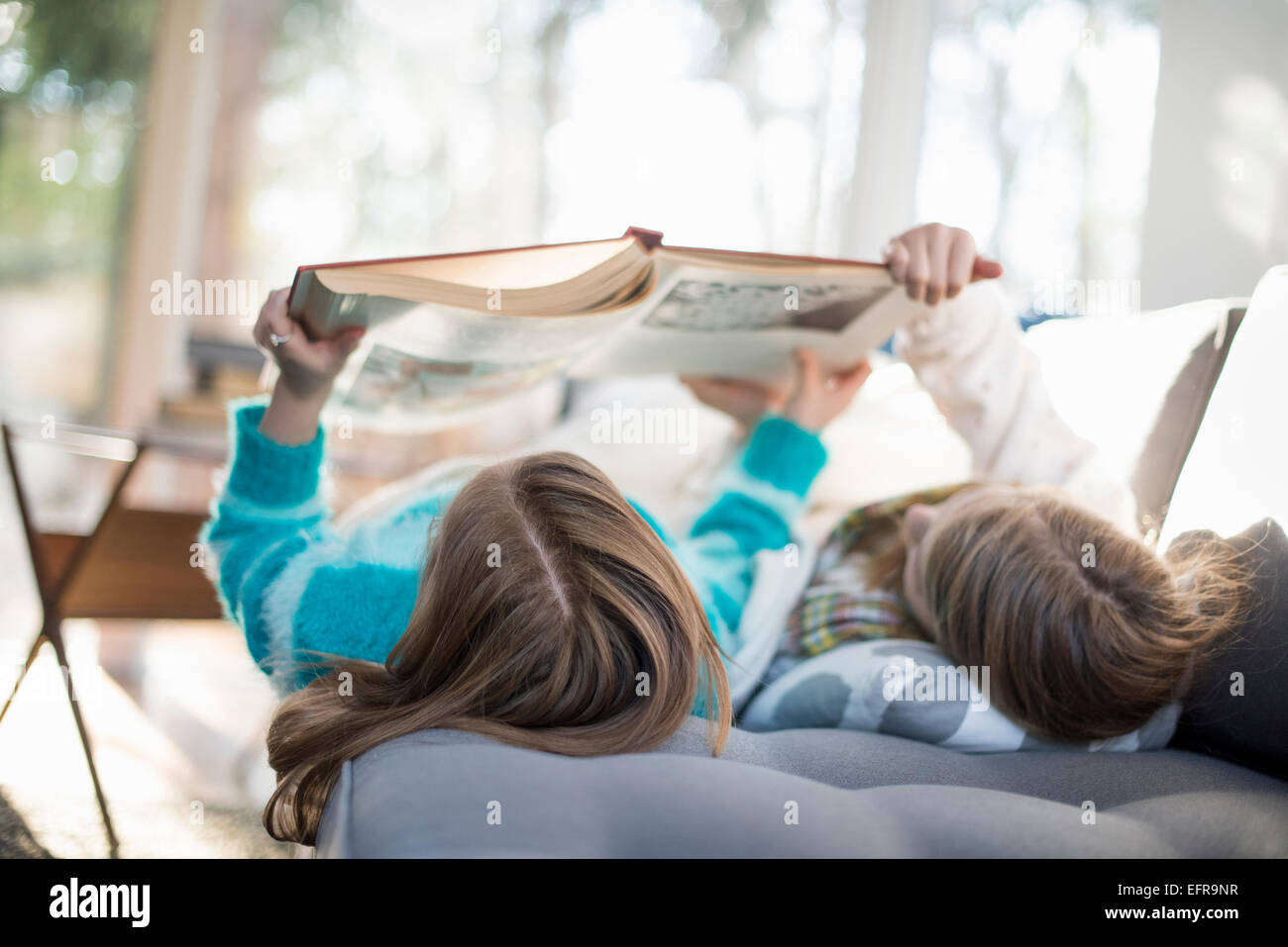 Two girls lying on a sofa on their back, reading a book. Stock Photo