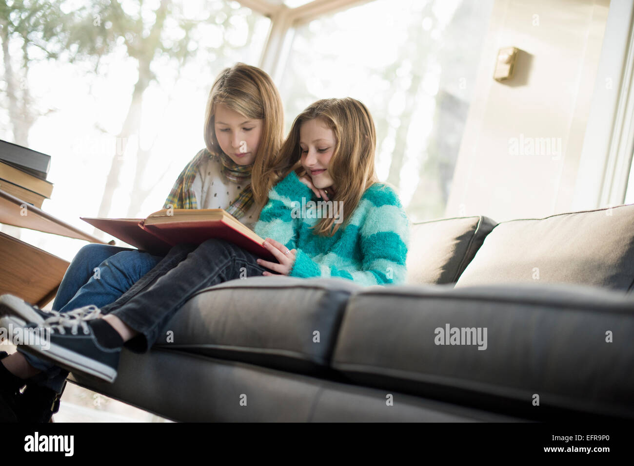 Two girls sitting on a sofa, reading a book. Stock Photo