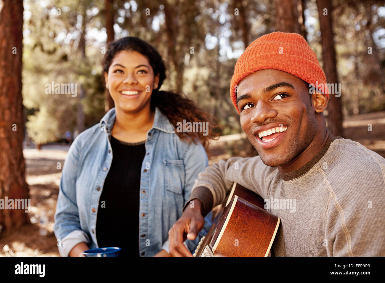 Young camping couple sitting in forest playing acoustic guitar Stock Photo