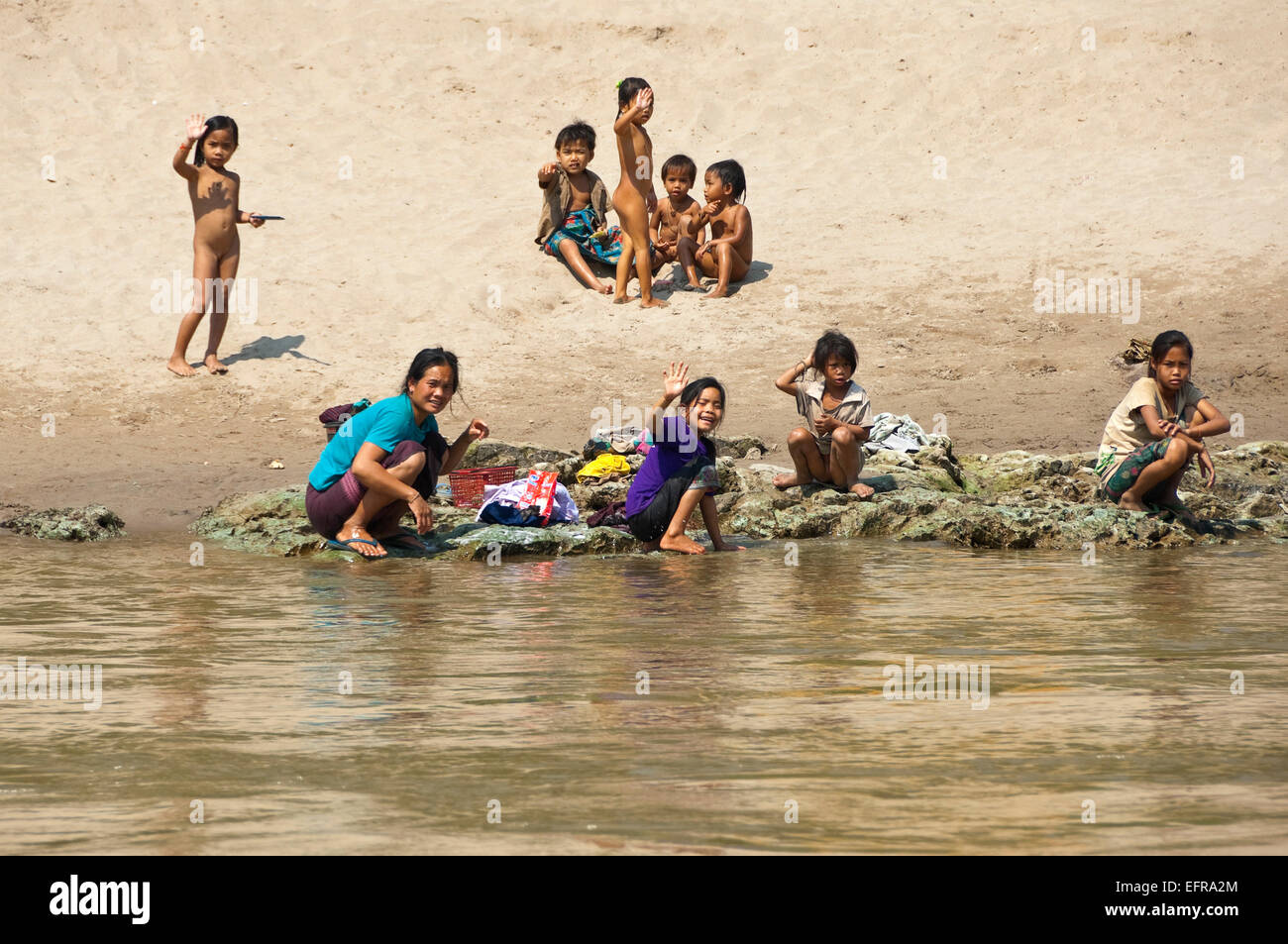 Horizontal view of a group of children playing and relaxing on the banks of the Mekong River. Stock Photo