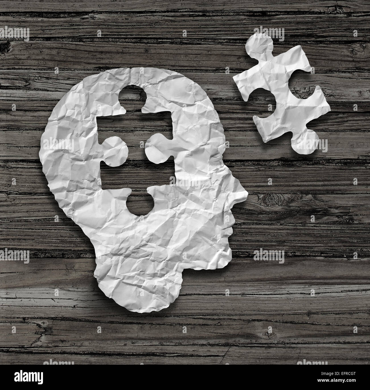 Puzzle head brain concept as a human face profile made from crumpled white paper with a jigsaw piece cut out on a rustic old wood background as a mental health symbol. Stock Photo